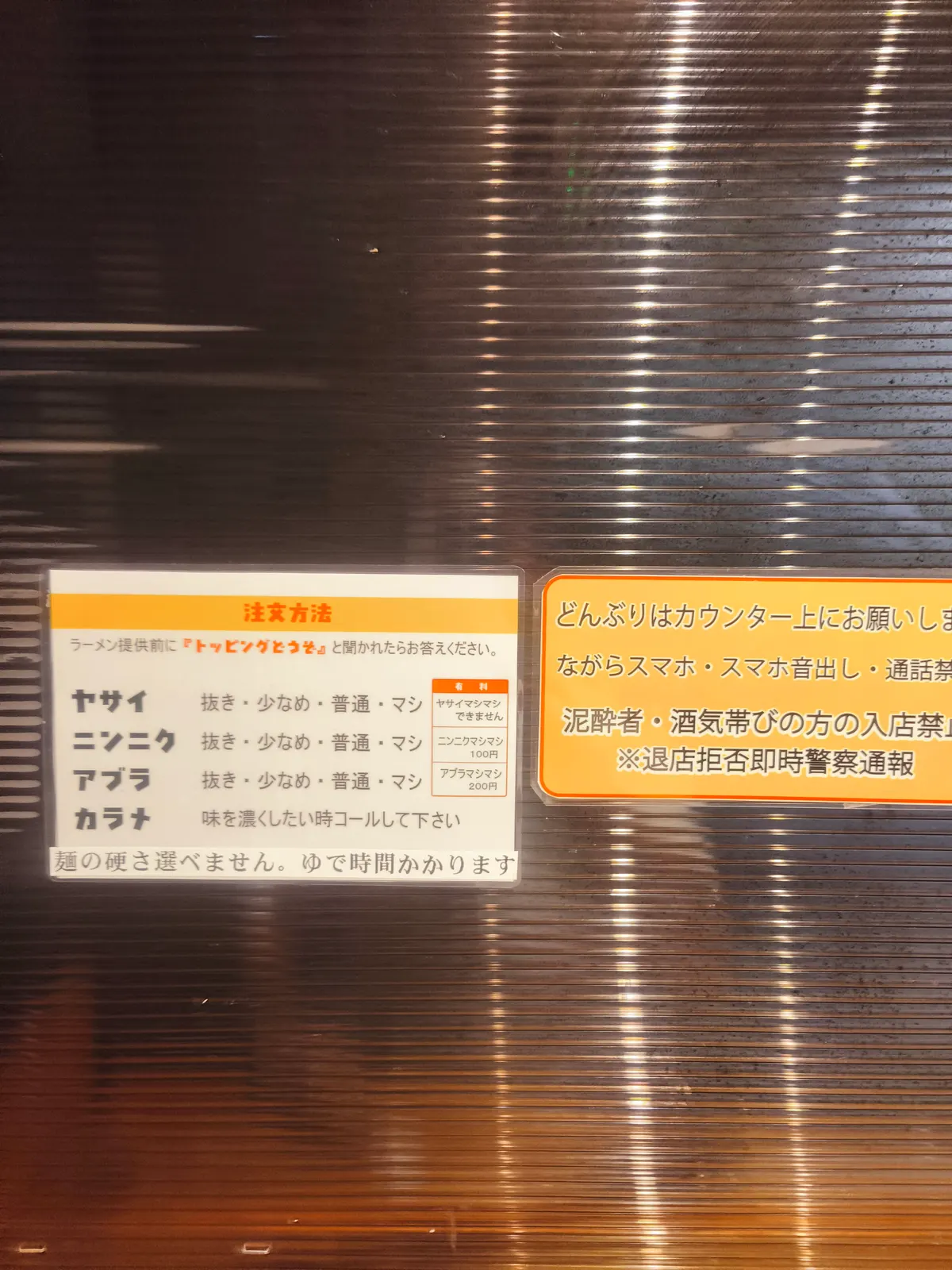 ブタゴリラの注文方法の貼り紙。ヤサイ・ニンニク・アブラを「抜き・少なめ・普通・マシ」から選ぶ案内。麺の硬さは選べず、茹で時間がかかる旨も書かれている