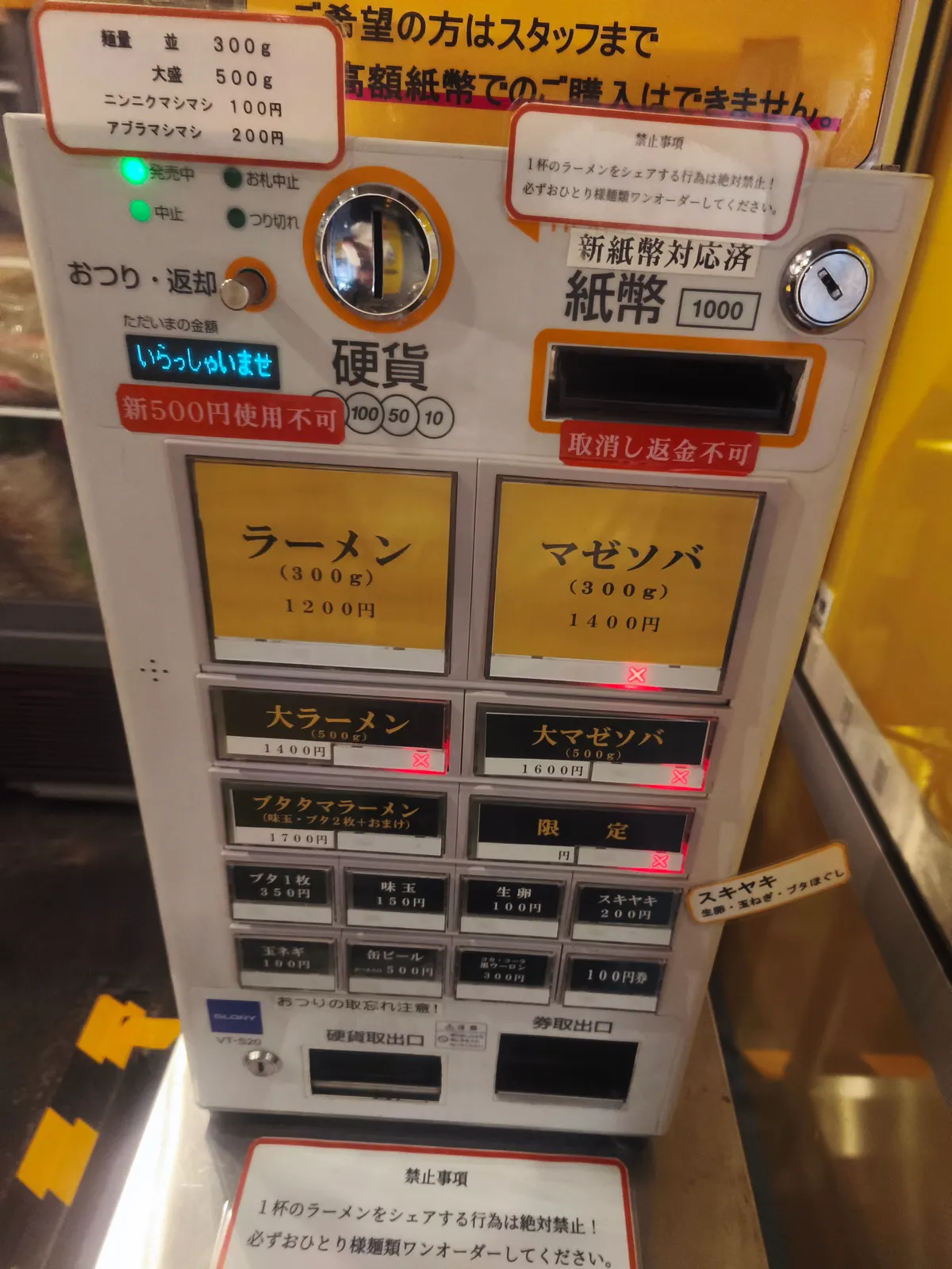 ブタゴリラの券売機。ラーメン300g 1,200円、マゼソバ300g 1,400円、ブタタマラーメン1,700円などのボタンが並ぶ。新500円硬貨は使用不可の表示もある