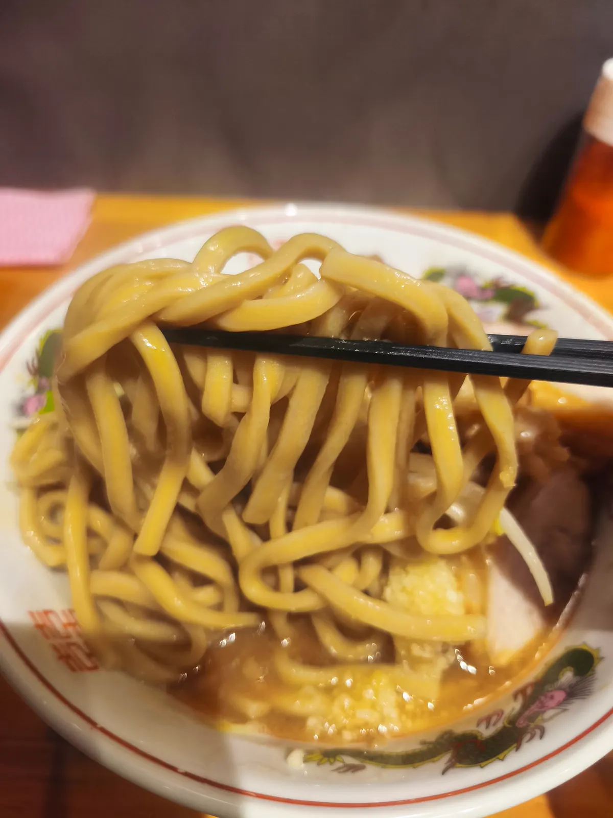 箸で持ち上げたブタゴリラの麺。淡い黄色で、うどんのように太くうねっている極太麺