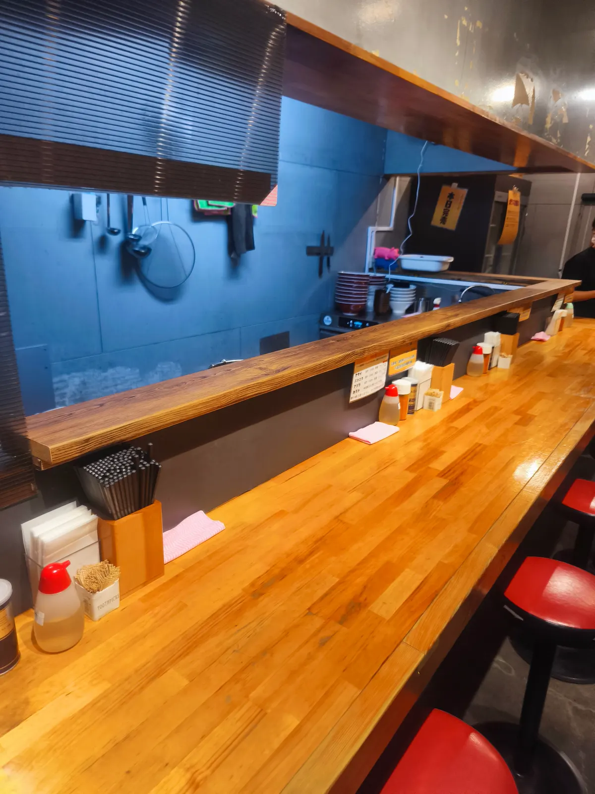 ブタゴリラの店内。木のカウンター席と赤いスツール、青い壁。卓上には調味料のボトルが並び、カウンター奥に丼が積まれている