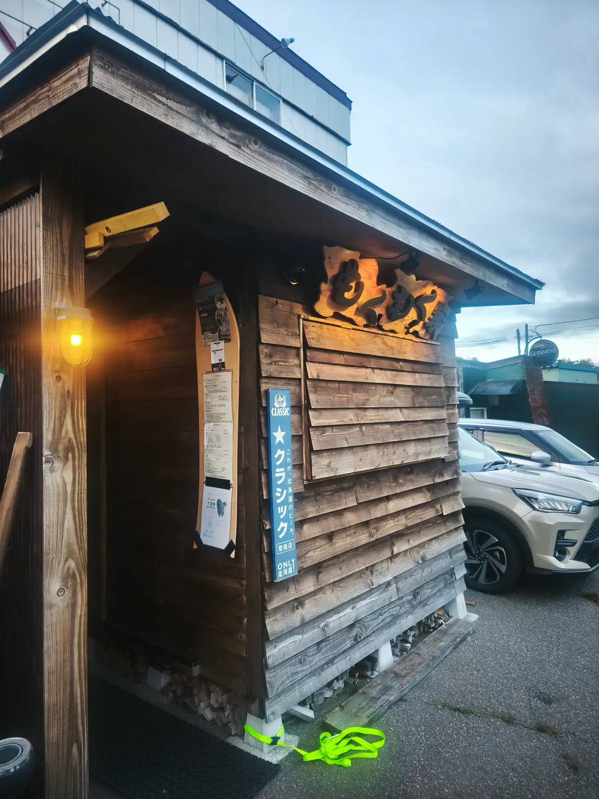 夕暮れの中、看板が明るく照らされたもくもく家の木造の店舗外観