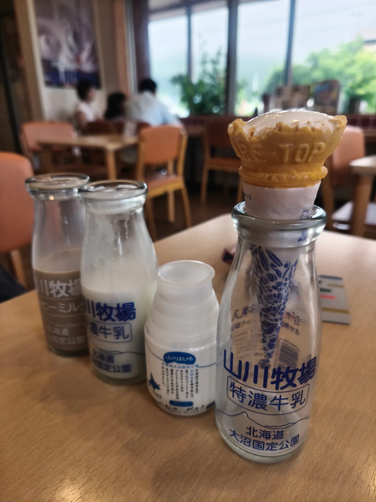 瓶入りの特濃牛乳・のむヨーグルト・コーヒーミルクと、トップに山川牧場のロゴ入りコーンが乗ったソフトクリーム