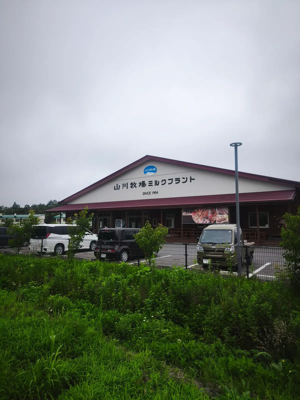 山川牧場ミルクプラントの建物外観と駐車場に停まった車