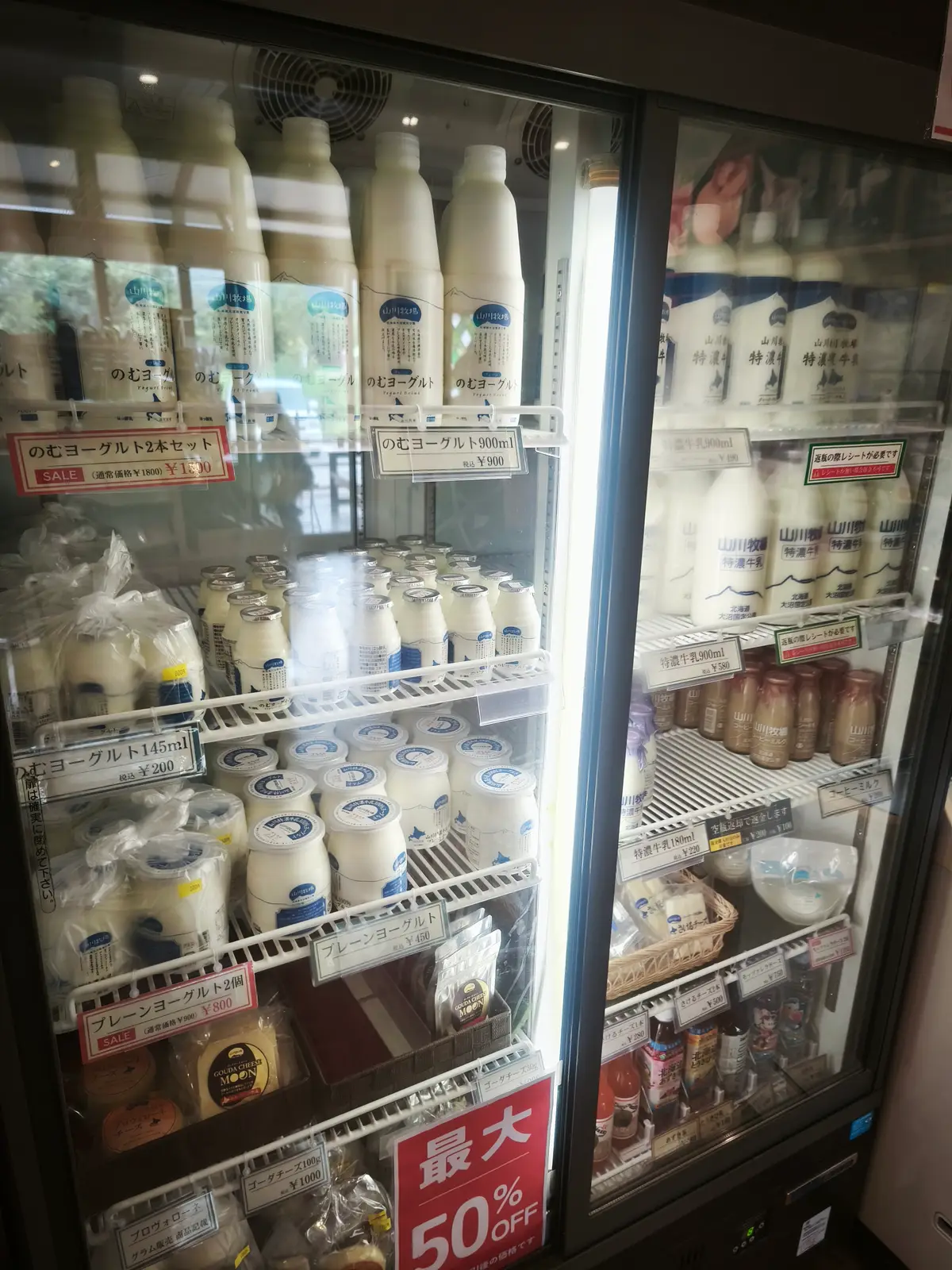 冷蔵ショーケースに並ぶのむヨーグルトや特濃牛乳、ゴーダチーズと値札