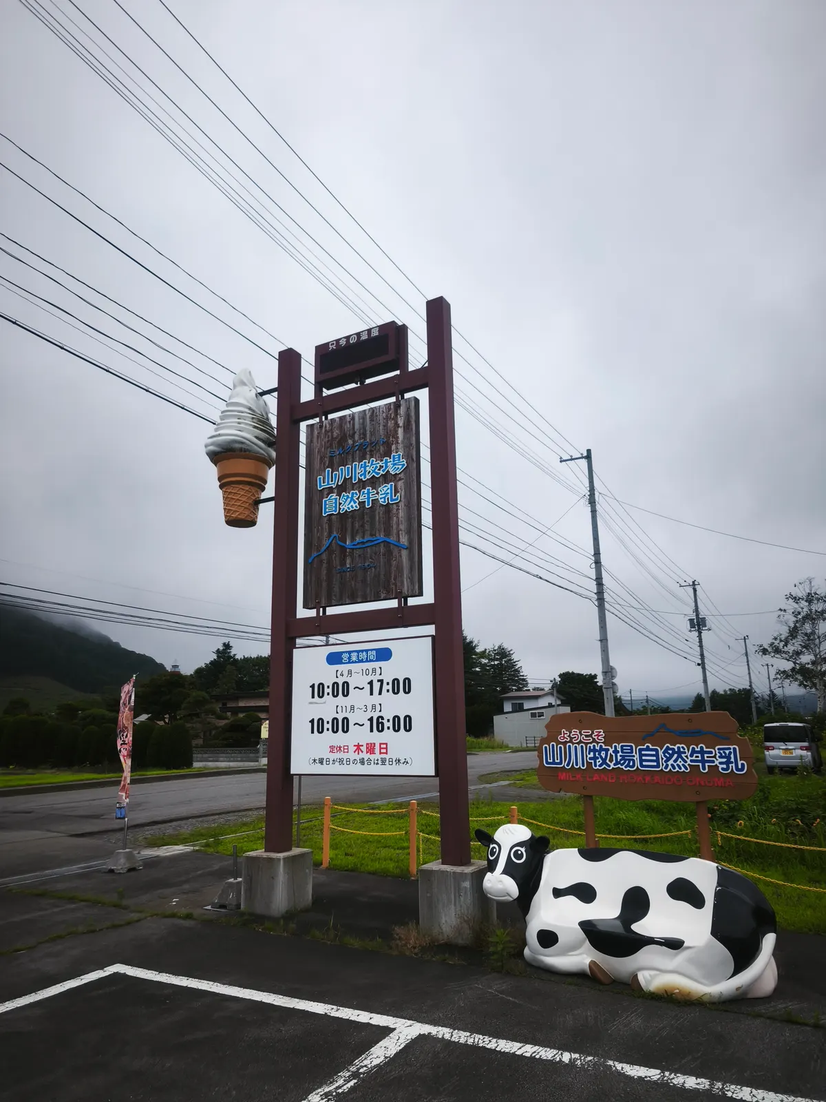 山川牧場自然牛乳の看板。営業時間4〜10月10:00〜17:00・11〜3月10:00〜16:00、定休日木曜日の表示とソフトクリームの模型