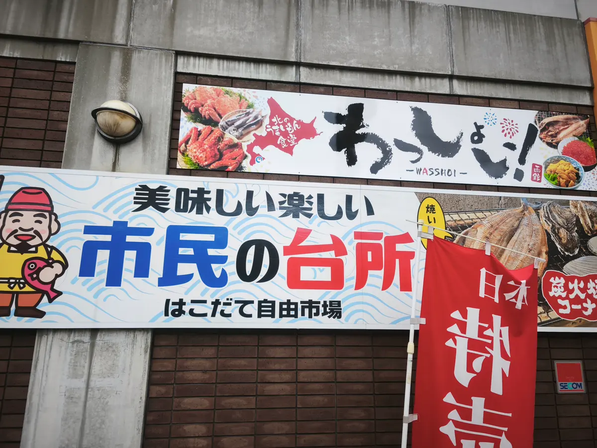 はこだて自由市場の外壁看板。「美味しい 楽しい 市民の台所 はこだて自由市場」と書かれている