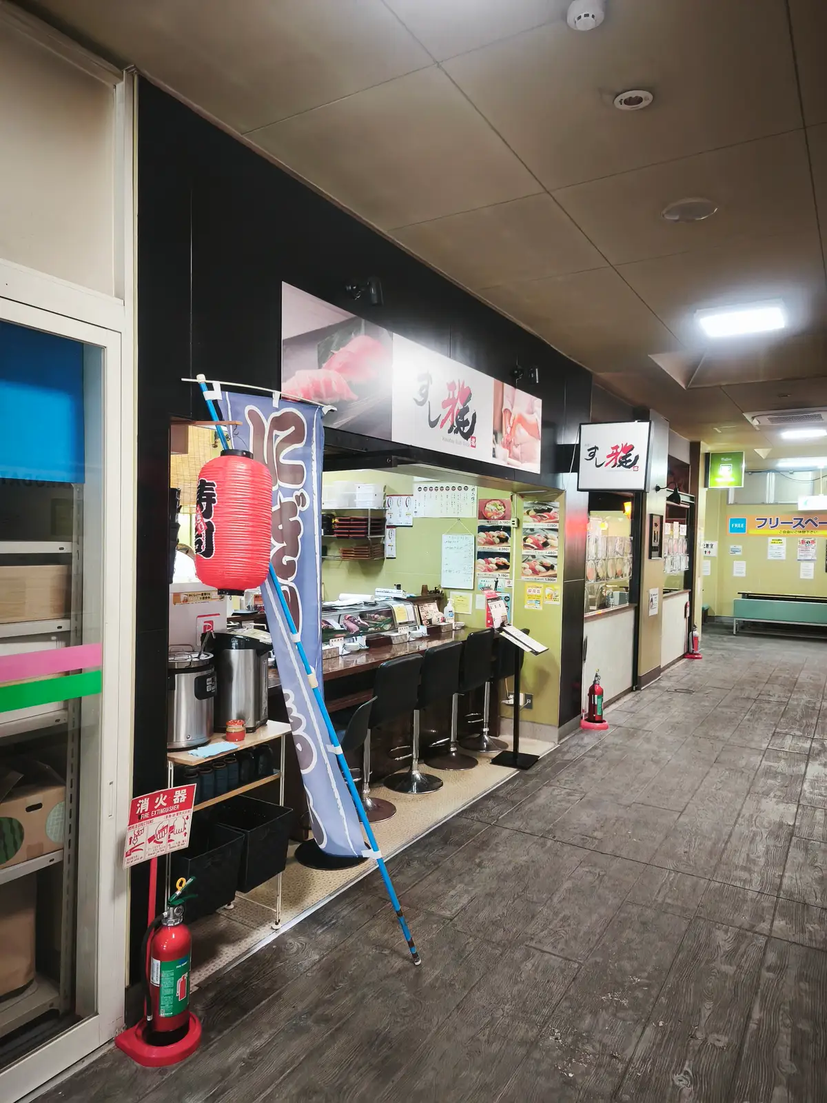 開店前のすし雅の店頭。カウンターの椅子が並び、通路には人がいない。奥に自由市場のフリースペースが見える