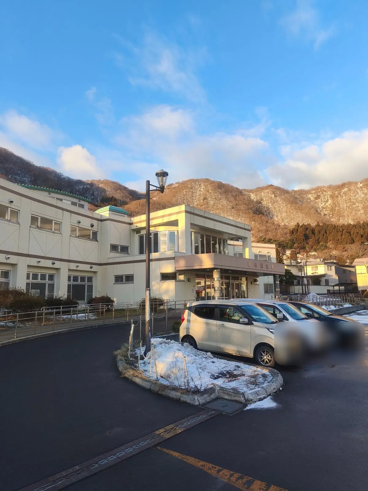 谷地頭温泉の外観。低層の建物の入口に「谷地頭温泉」の看板があり、背後に山が見える