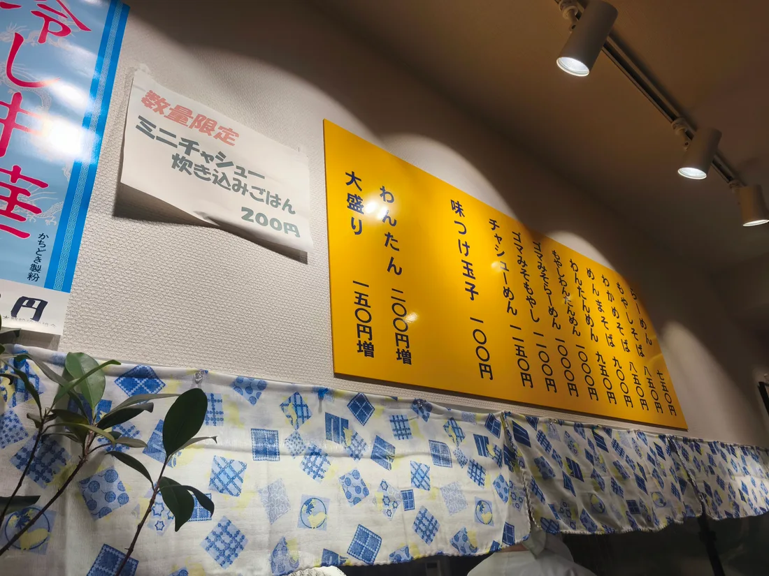 かいらくのメニュー表。「数量限定 ミニチャーシュー炊き込みごはん 200円」の貼り紙と、黄色い品書き。わんたん200円増、大盛り150円増、味つけ玉子100円などの表記が見える